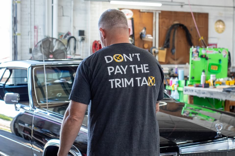 The Don't Pay the Trim Tax tee, worn in the shop next to a classic black car